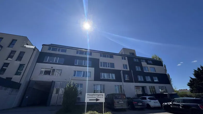 Mehrstöckiges Gebäude mit moderner Fassade und Parkplätzen unter strahlendem Sonnenschein.