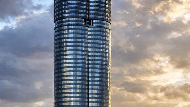 Moderner, zylindrischer Wolkenkratzer mit Glasfassade am Wasser, unter einem dramatischen Himmel bei Sonnenuntergang.
