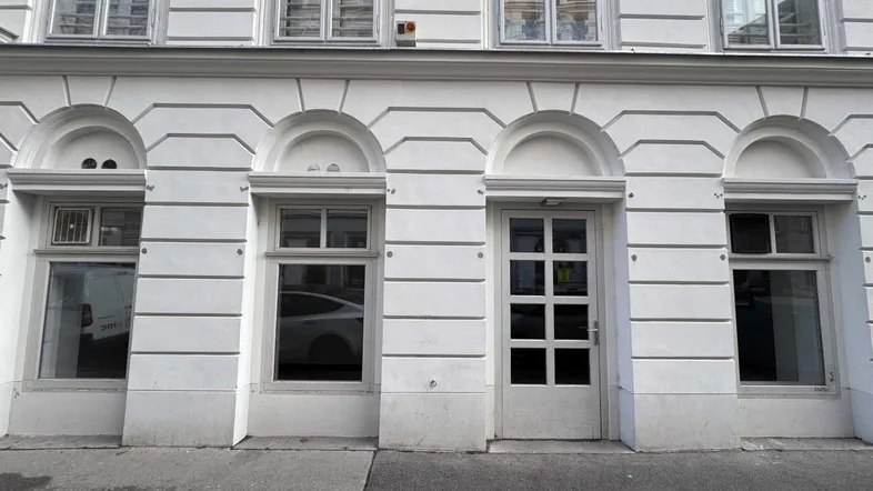 Nahaufnahme der weiß gestrichenen Fassade eines Altbaus mit Fenstern und einer Eingangstür im Erdgeschoss.