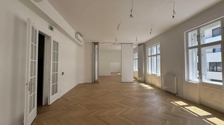 Geräumiger, heller Büroraum mit elegantem Fischgrätparkett, hohen Fenstern und Klimaanlage.