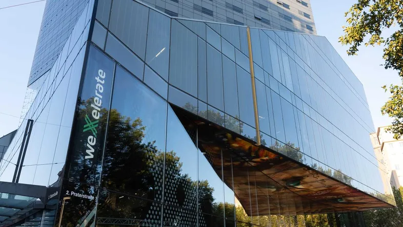 Modernes Gebäude mit Glasfassade und einem höheren Hotelturm im Hintergrund in einer städtischen Umgebung.