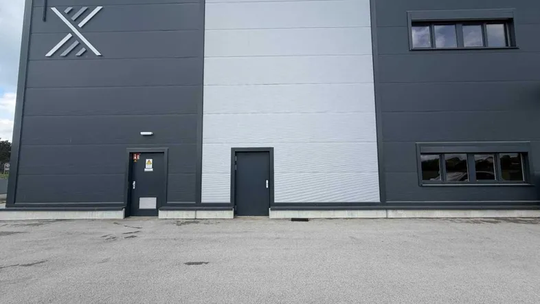Moderne Fassade eines Industriegebäudes mit dunklen und hellen Paneelen sowie mehreren Türen und Fenstern.