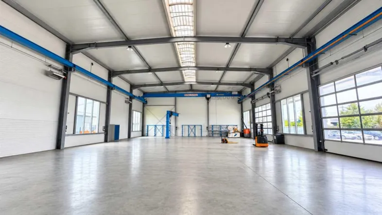 Geräumige und helle Lagerhalle mit hohen Decken, Betonboden und großen Fenstern, ideal für industrielle Nutzung.