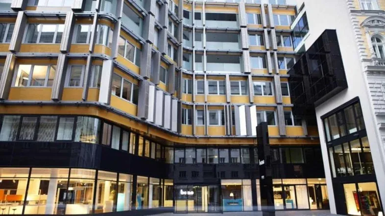 Moderne Bürogebäude-Fassade mit gelben und grauen Elementen sowie großen Glasflächen im Erdgeschoss.