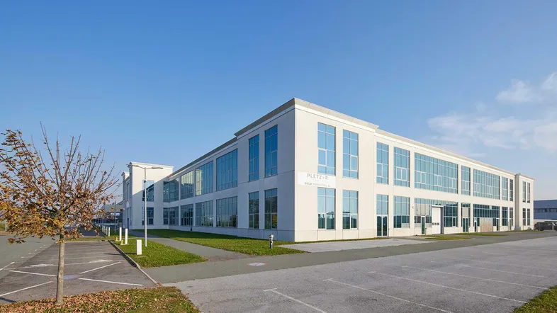 Modernes Bürogebäude mit großen Fenstern und Parkplätzen unter blauem Himmel.
