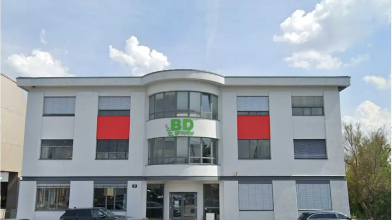 Gebäudeansicht eines modernen Bürokomplexes mit Firmenlogo und Parkplätzen davor.