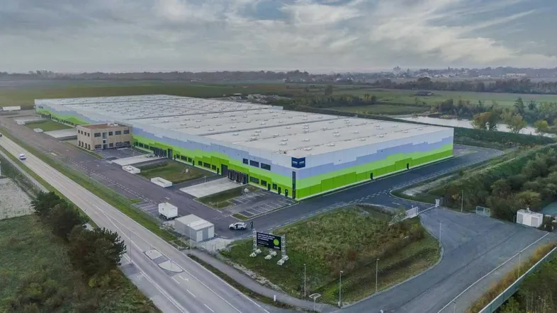Luftaufnahme eines großen modernen Logistikzentrums mit weitläufigen Parkplätzen und umliegenden Grünflächen.