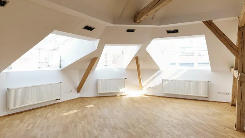 Heller Dachbodenraum mit sichtbaren Holzbalken, großen Dachfenstern und Parkettboden.