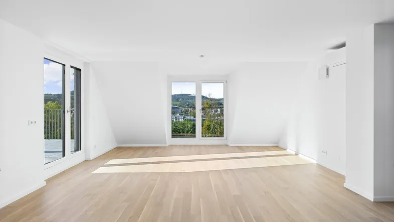 Helles Wohnzimmer mit Holzboden, Dachschrägen und Zugang zu französischen Balkonen.