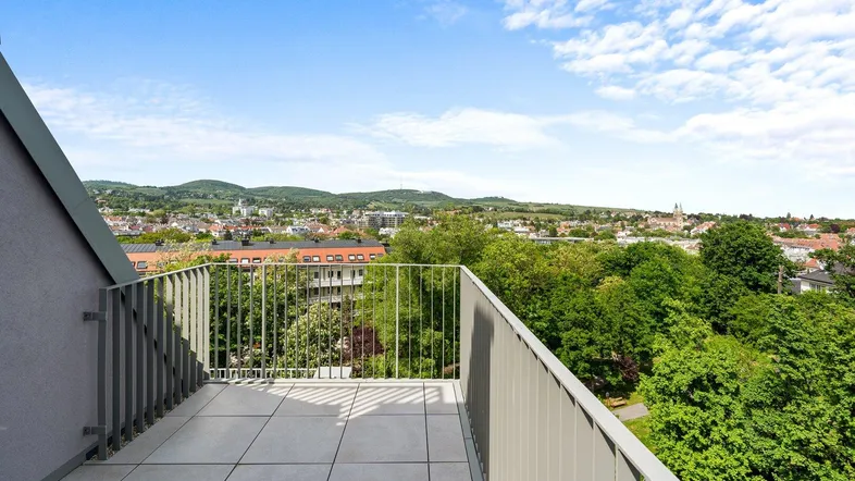 Geräumiger Balkon mit Fliesenboden und weitem Blick über die Stadt und grüne Hügel.