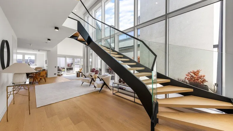 Helles Wohnzimmer mit moderner Treppe, hohen Decken und großen Fenstern, die viel Licht hereinlassen.