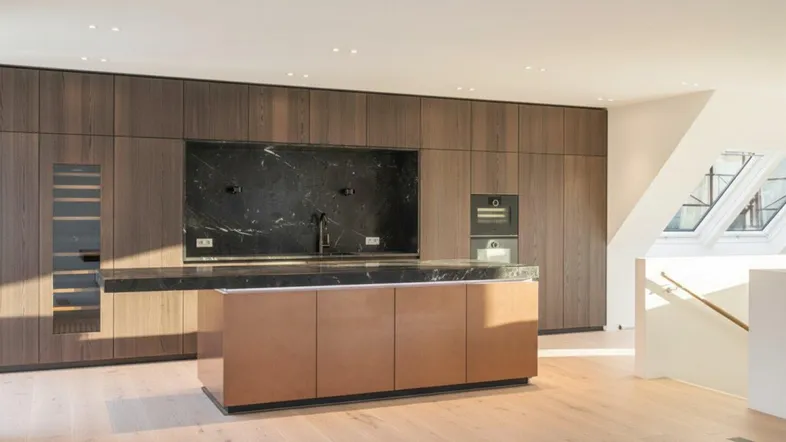 Moderne Küche mit dunklen Holzfronten, Marmorarbeitsplatte und integrierten Geräten unter Dachschräge.