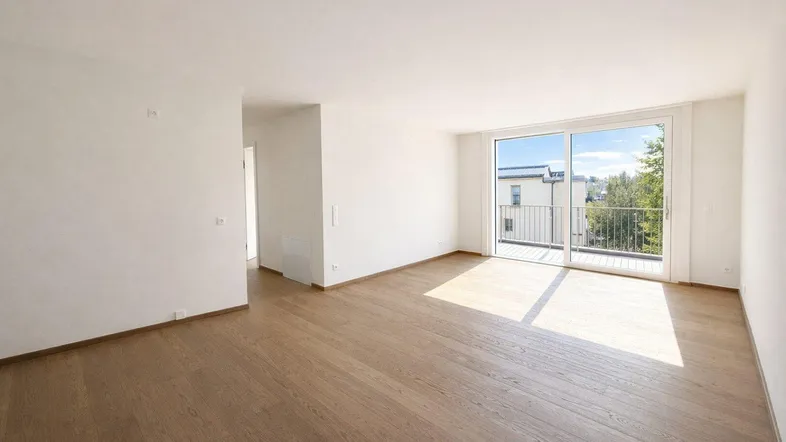 Heller, leerer Wohnbereich mit Holzboden und großen Schiebetüren zum Balkon.
