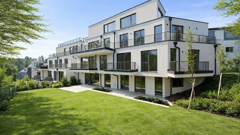 Modernes Mehrfamilienhaus mit weißer Fassade, Balkonen und großzügiger Grünfläche in sonniger Lage.