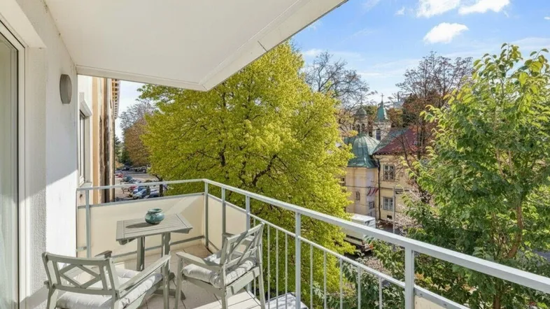 Heller Balkon mit Sitzgelegenheiten und weitem Blick auf grüne Bäume und historische Gebäude der Stadt.
