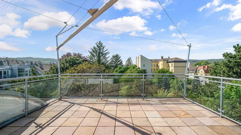 Geräumige Dachterrasse mit Fliesenboden, Glasgeländer und weitem Blick ins Grüne.