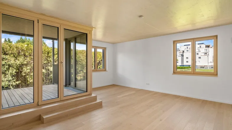 Helles Zimmer mit Holzboden und Zugang zu einem Balkon, bietet Blick auf die Umgebung.