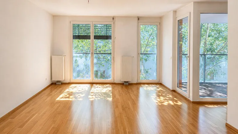 Helles Wohnzimmer mit Parkettboden, großen Fenstern und Zugang zu einem Balkon.