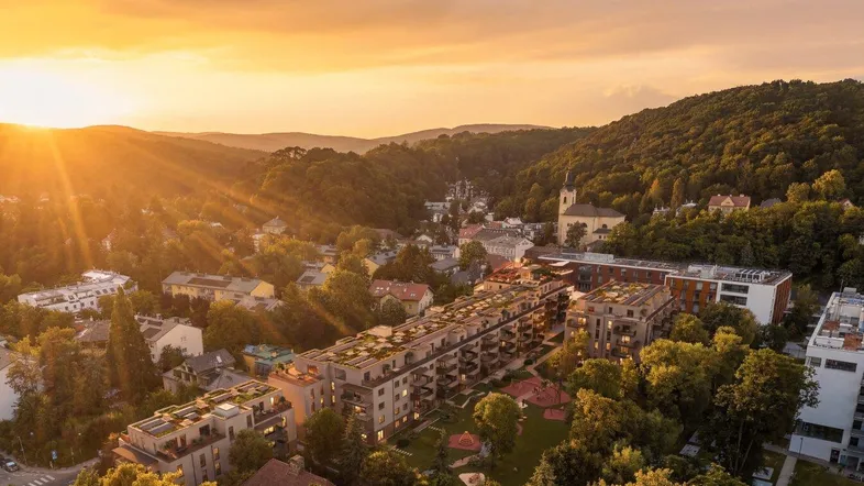 Luftaufnahme einer Wohnanlage in hügeliger Landschaft bei Sonnenuntergang mit warmem Licht.