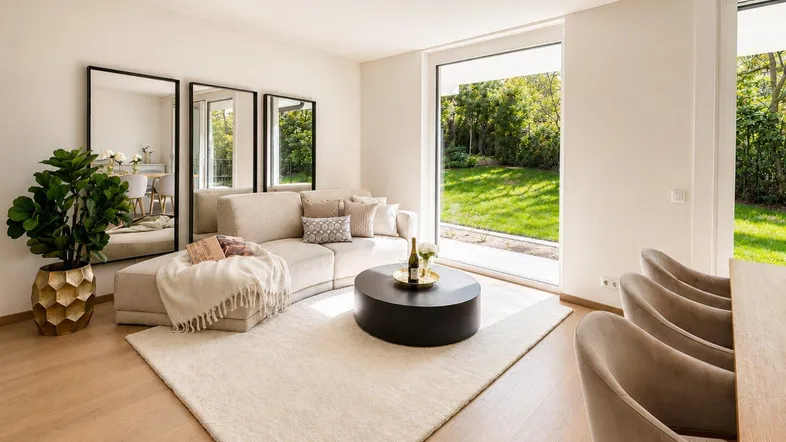 Helles Wohnzimmer mit beigem Sofa, Holzboden und großen Fenstern zum Garten.