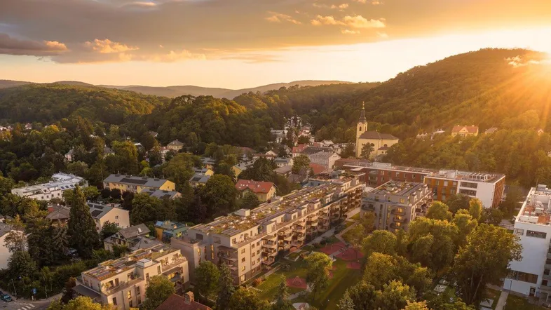 Malerische Luftaufnahme einer Stadt mit Wohngebäuden und grünen Hügeln bei Sonnenuntergang.