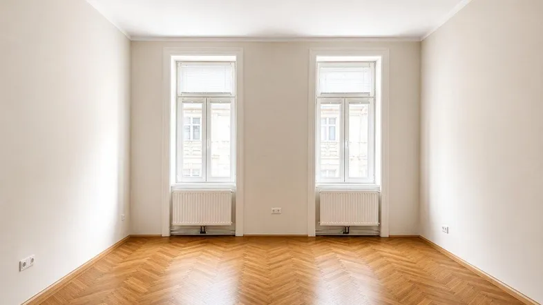 Geräumiges Zimmer mit klassischem Fischgrätparkett und viel Tageslicht durch zwei große Fenster.