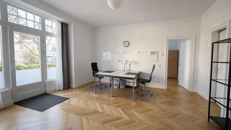 Helles Büro mit Fischgrätparkett und großen Fenstern, die viel Tageslicht hereinlassen.