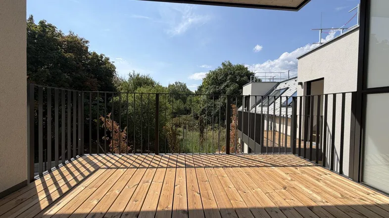 Geräumiger Balkon mit Holzboden und Blick ins Grüne, ideal für entspannte Stunden im Freien.