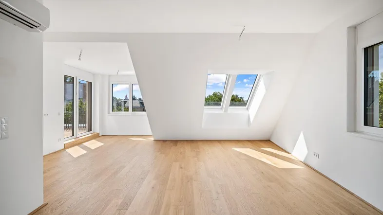 Helles Dachgeschosszimmer mit Holzboden, Dachfenstern und Zugang zu einem kleinen Balkon.