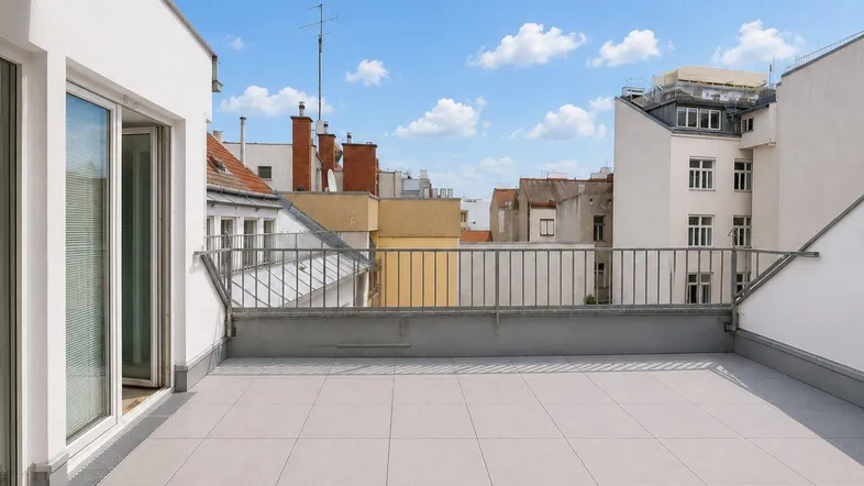 Große, geflieste Dachterrasse mit Metallgeländer und Blick auf die umliegenden Gebäude der Stadt.