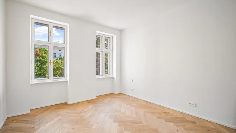 Heller Raum mit Fischgrätparkett und hohen Decken, ideal als Wohn- oder Schlafzimmer.
