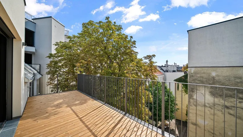 Geräumige Terrasse mit Holzboden und Metallgeländer, umgeben von Bäumen und Stadtblick.