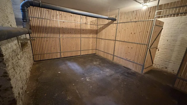 Kellerabteil mit Holzabtrennungen, sichtbaren Rohren und robustem Betonboden.
