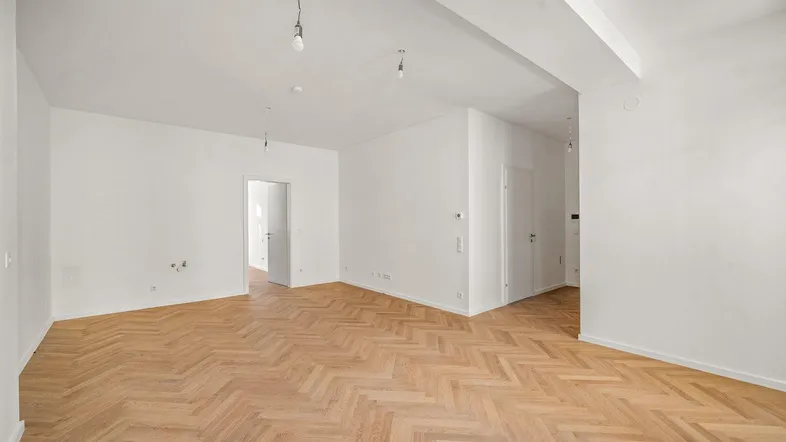 Helles, leeres Zimmer mit Fischgrätparkett und weißen Wänden, bereit zur individuellen Gestaltung.