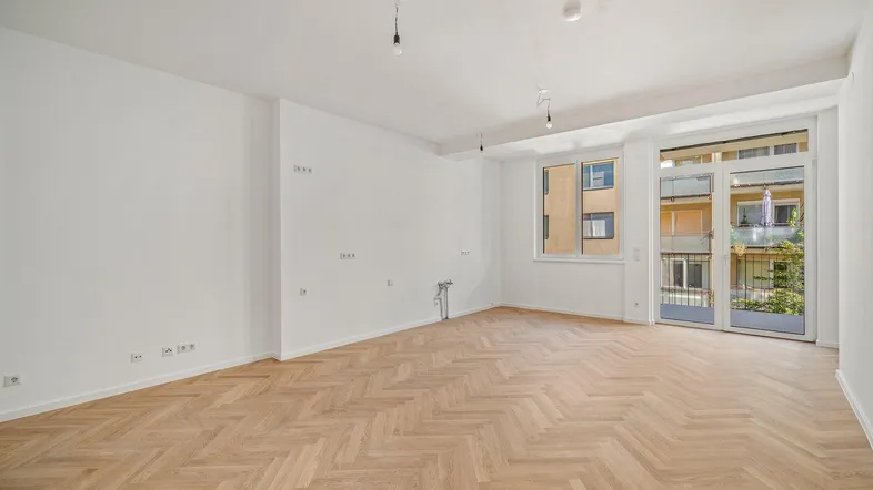 Heller Wohnraum mit Fischgrätparkettboden und Zugang zu einem Balkon, ideal für moderne Einrichtung.