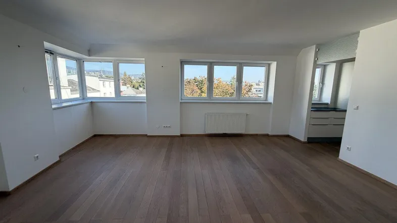 Helles Wohnzimmer mit Parkettboden und vielen Fenstern, die viel Tageslicht hereinlassen.