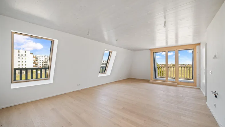 Helles, geräumiges Wohnzimmer mit Holzboden, Dachschrägen und Zugang zum Balkon.