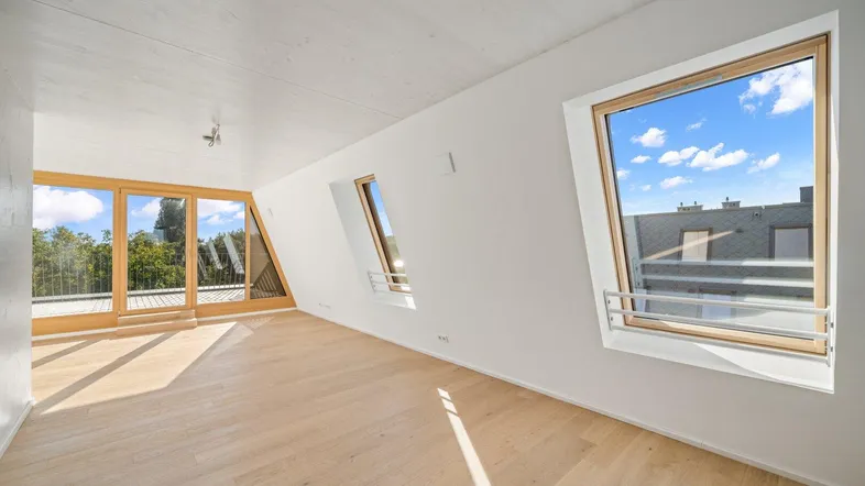 Heller Dachgeschossraum mit Holzboden und großen Fenstern, die viel Tageslicht hereinlassen.