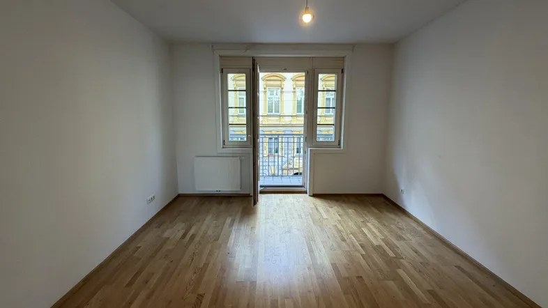 Heller Raum mit Parkettboden und Zugang zu einem kleinen Balkon, ideal als Wohnzimmer.