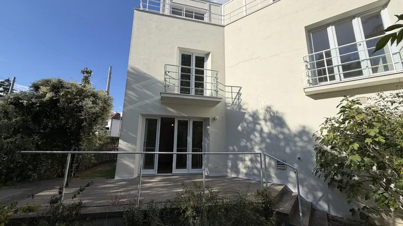 Moderne Hausfassade mit weißem Putz, einer Terrasse im Erdgeschoss und einem kleinen Balkon.