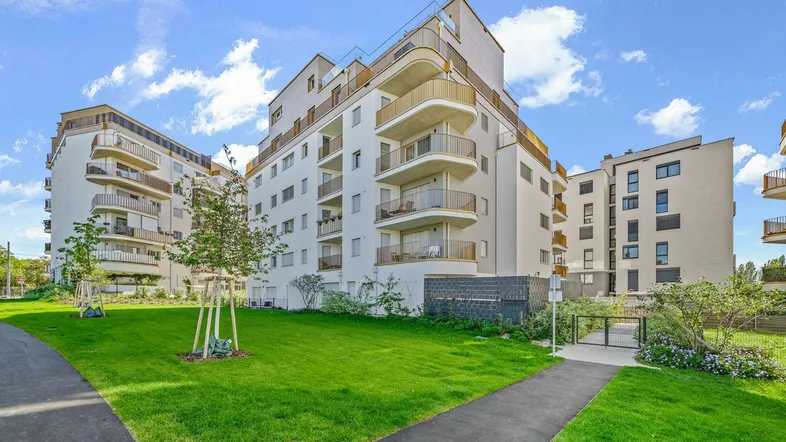 Moderne Wohngebäude mit Balkonen und gepflegten Grünflächen unter blauem Himmel.