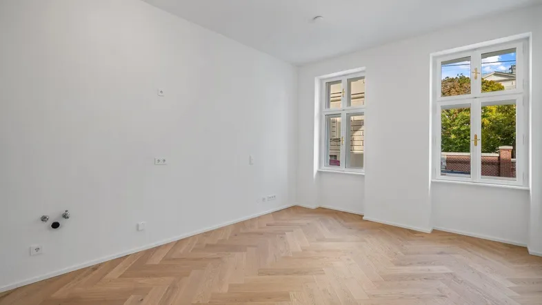 Helles, leeres Zimmer mit Fischgrätparkett und großen Fenstern, bereit zur individuellen Gestaltung.