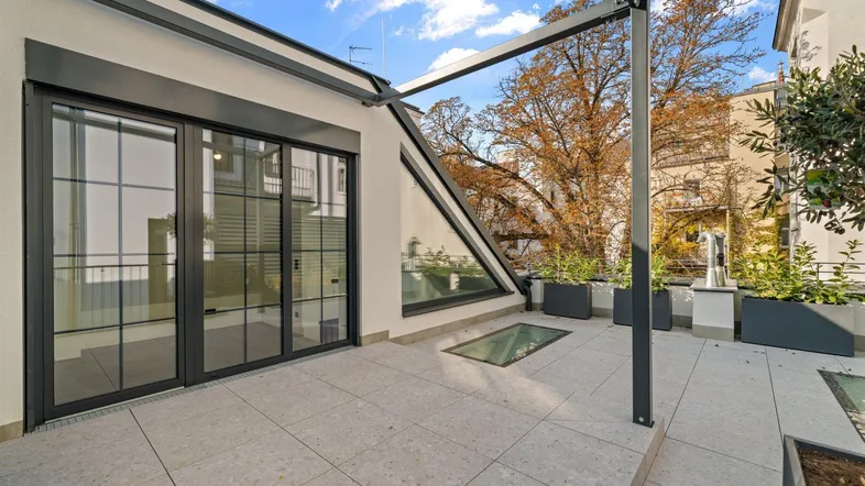Geräumige Dachterrasse mit modernen Fliesen, Glasdachfenstern und Blick auf die Umgebung.