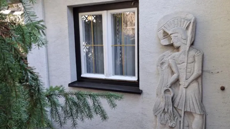 Fenster mit dunklem Rahmen und einer dekorativen Steinstatue an der Hauswand.