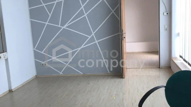 Leerer Büroraum mit modern gestalteter Wand, Laminatboden und abgehängter Decke.