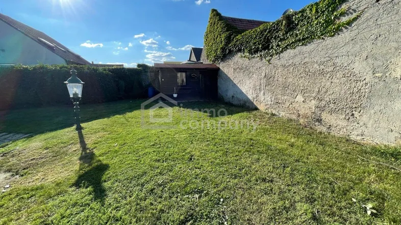 Sonnige Gartenfläche mit Rasen und einer alten Steinmauer, ideal für Entspannung im Freien.