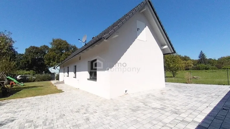 Modernes Einfamilienhaus mit weißer Fassade, dunklem Dach und gepflasterter Zufahrt unter blauem Himmel.