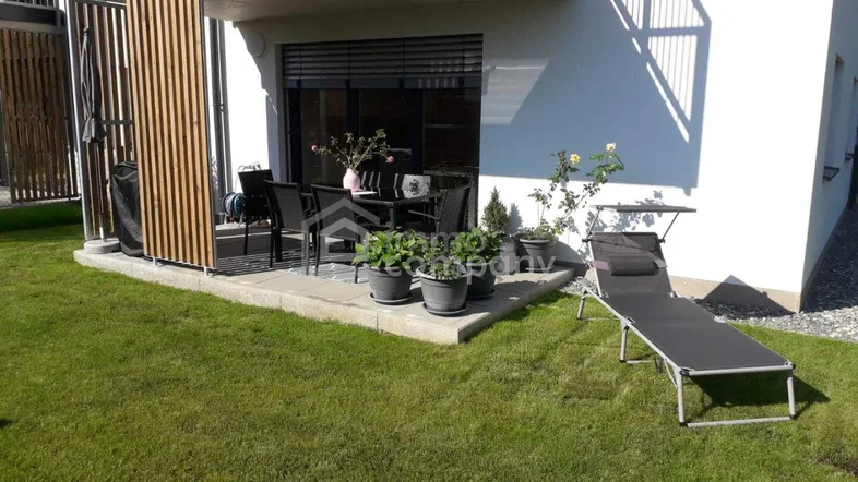 Sonnige Terrasse mit Gartenmöbeln und Liegestuhl, umgeben von einer gepflegten Rasenfläche.