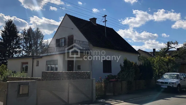 Einfamilienhaus mit Satteldach, kleinem Balkon und Vorgarten unter blauem Himmel.