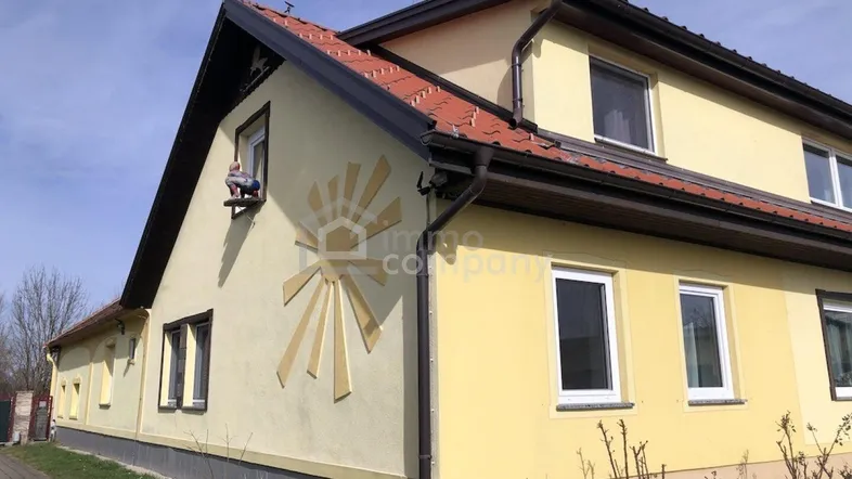Gelbe Hausfassade mit braunem Dach und Regenrinnen unter blauem Himmel.